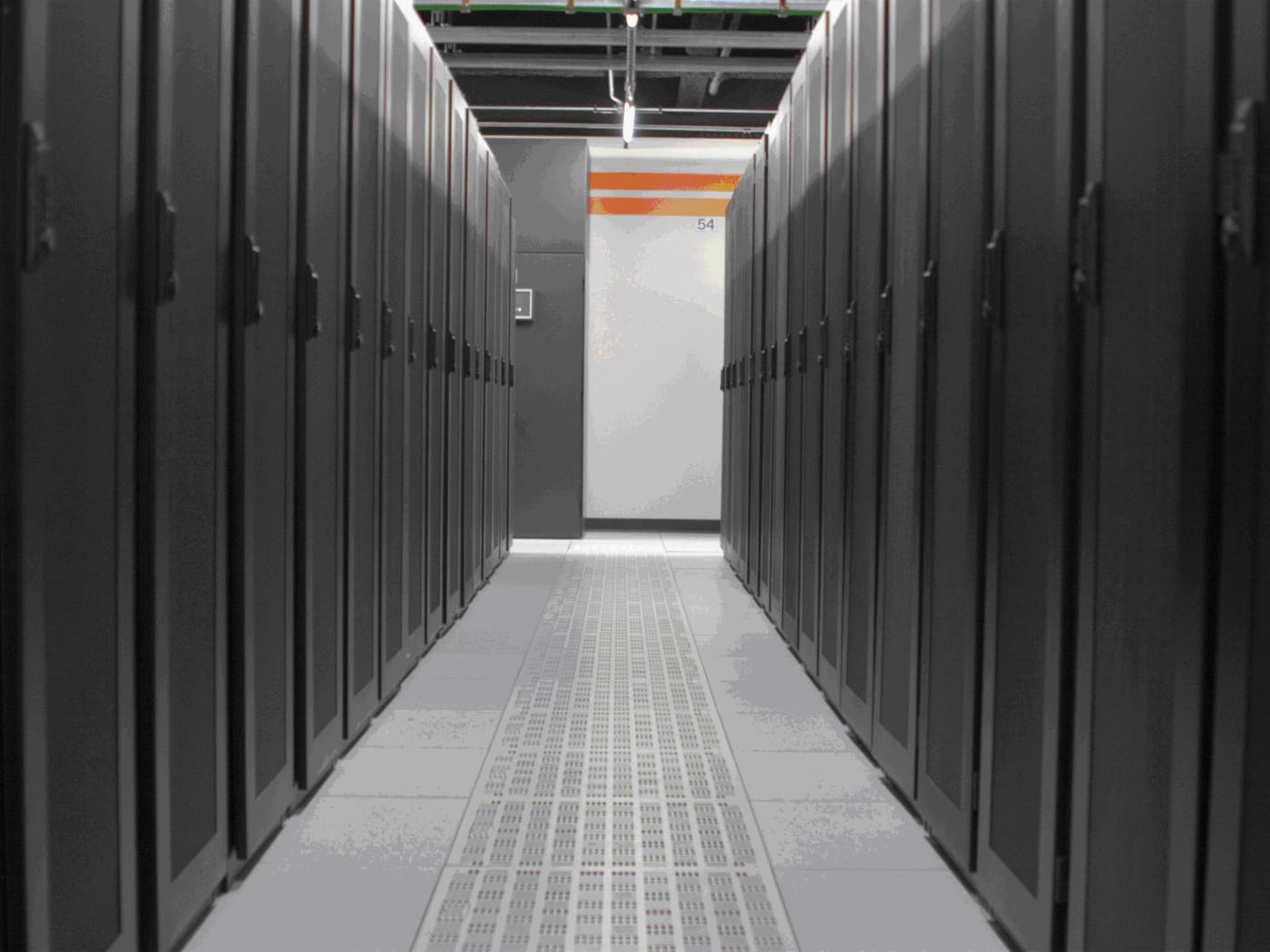 Aisle between rows of dark racks in a data center, with a perforated raised floor