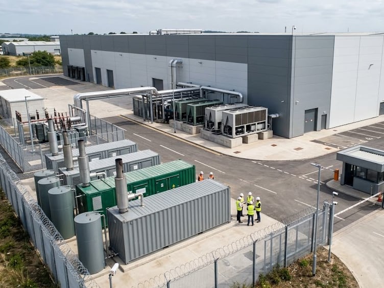Aerial view of a new data center campus: gray building, chillers, containerized generators, a substation and a crew in hard hats and vests in the fenced yard